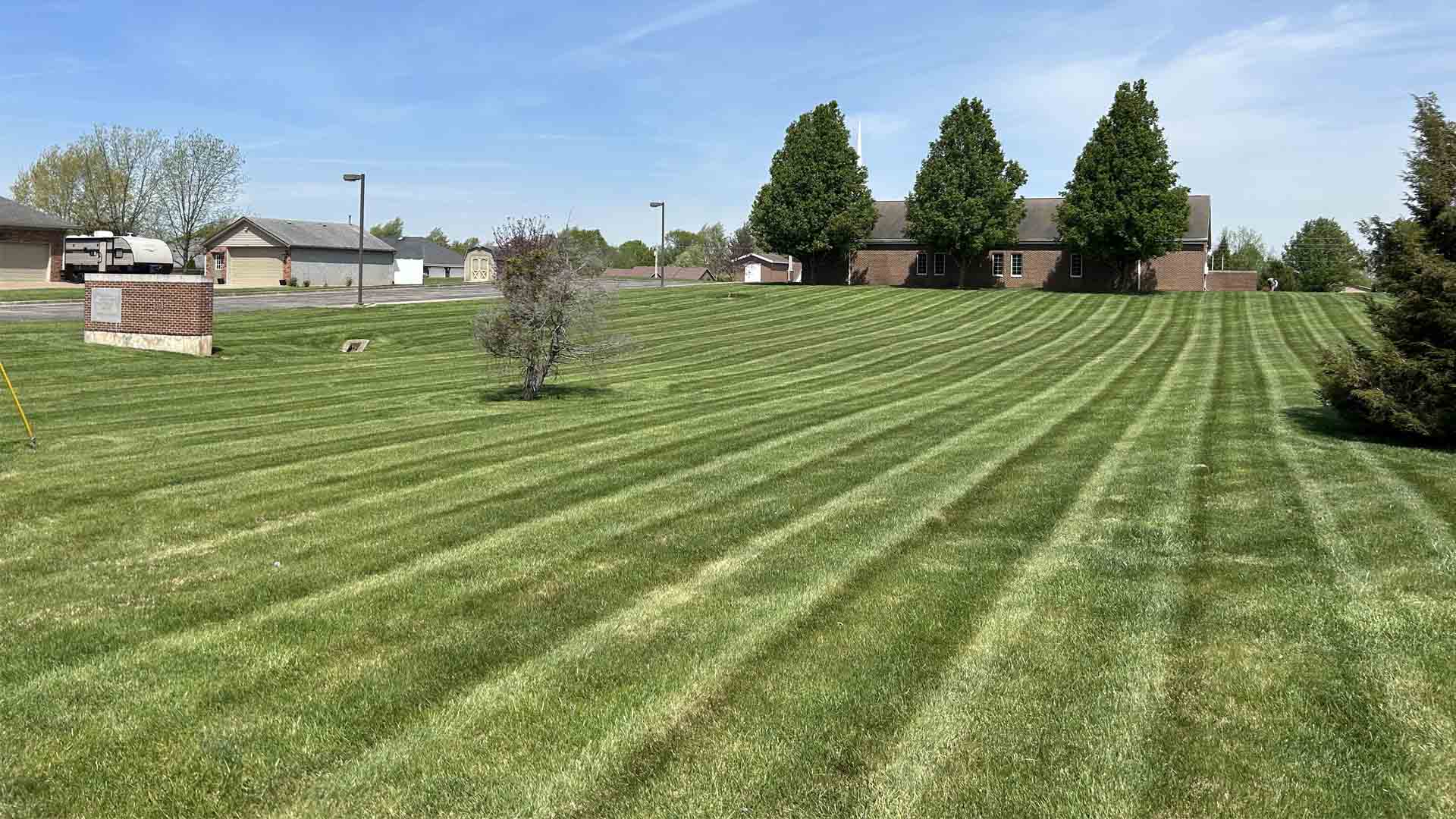 Refined landscaping touch meticulously striped lawn leads toward brick building sunny day blue sky visible.