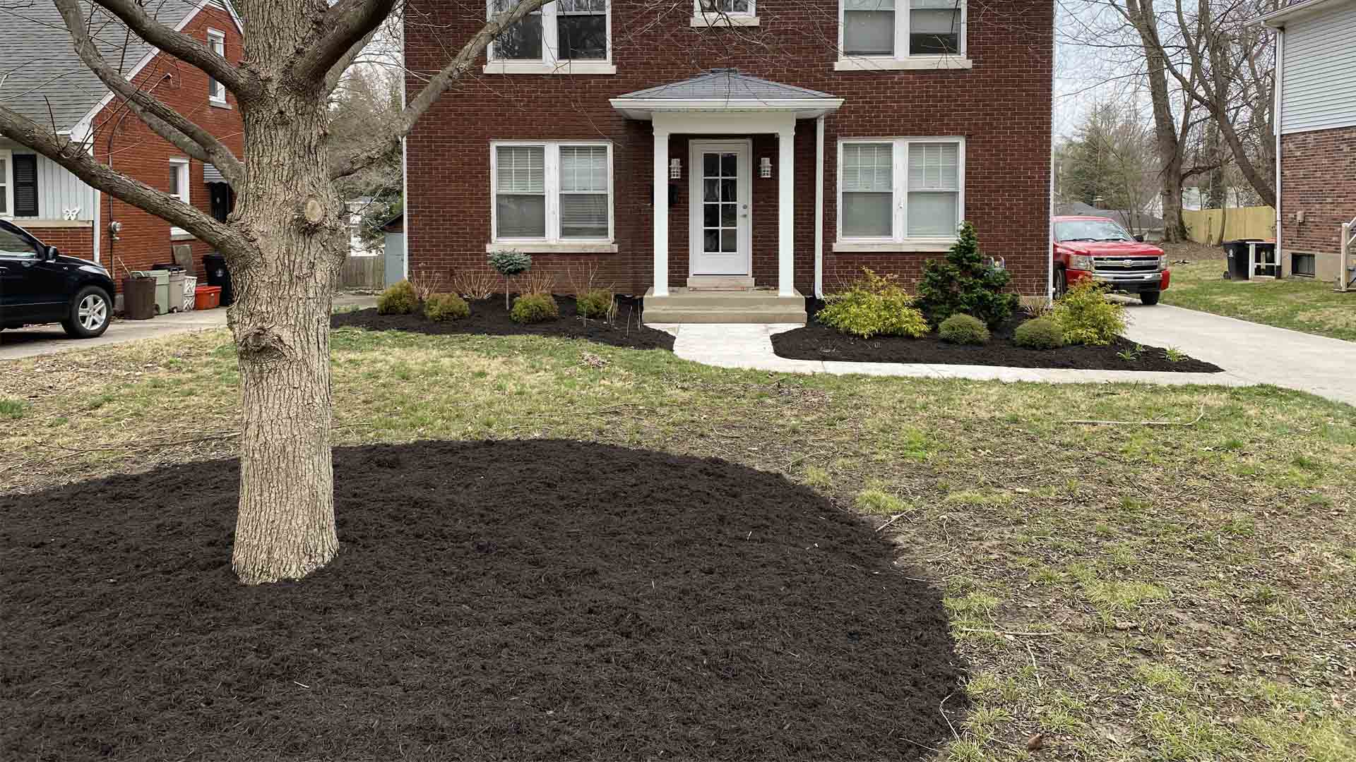 Freshly mulched garden beds and tree base enhance curb appeal in front of a brick home.