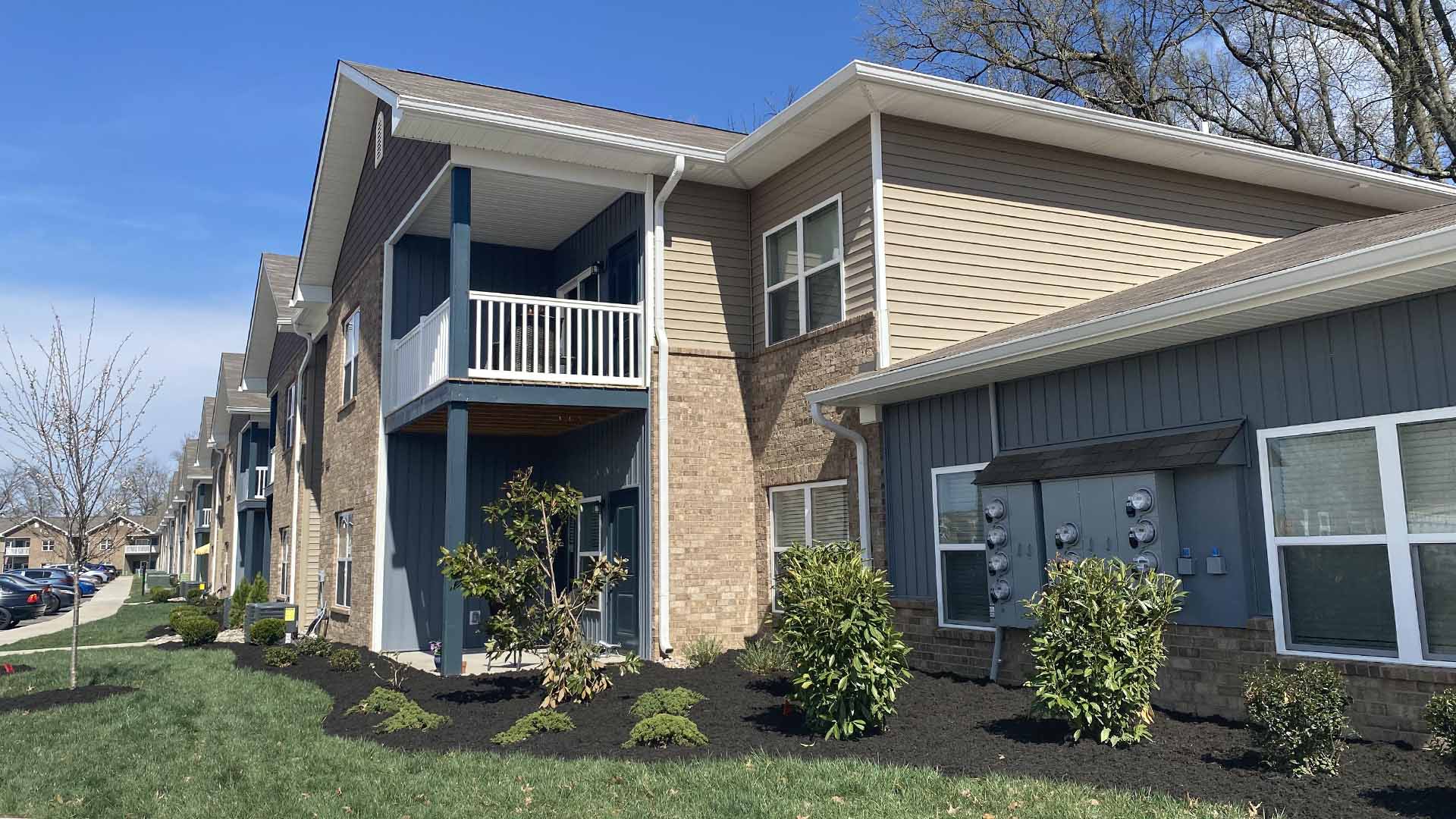 Breathtaking landscaping custom designed beds surround apartment building, premium mulch highlights exquisite grounds, cars visible nearby.