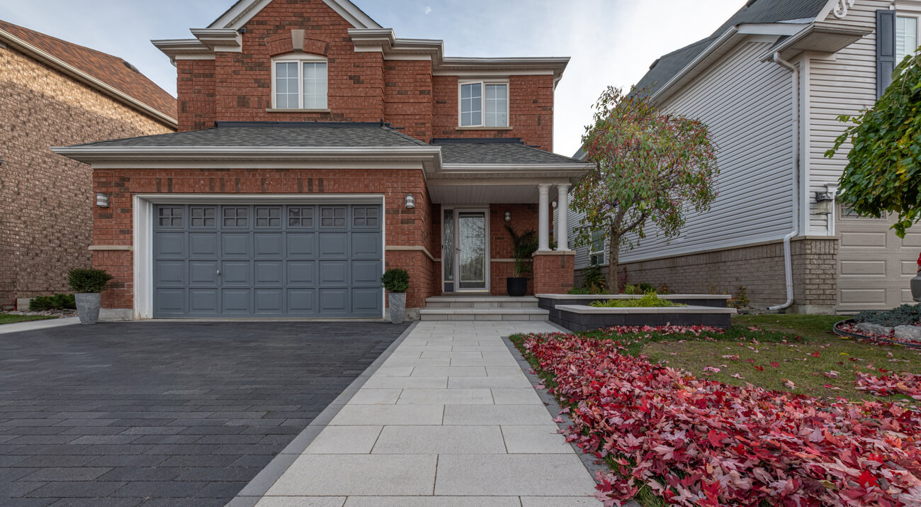 Contemporary home with custom dark paver driveway and light walkway, bordered by red autumn leaves and landscaping.